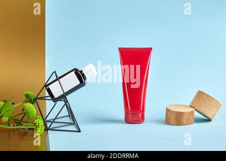 Tubo cosmetico rosso senza logo, supporti in legno, bottiglia di plastica su figurine di fiori verdi e triangolari, sfondo colorato. Primo piano, spazio di copia Foto Stock