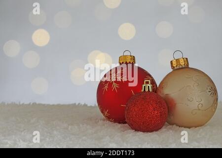Tre lampadine ornamentali natalizie sono mostrate su una superficie bianca simile alla neve e poste di fronte a un bokeh di luci rotonde, con spazio per la copia. Foto Stock