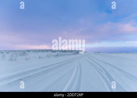Cingoli pneumatici su strade coperte di neve in un paesaggio artico Sotto un cielo nuvoloso della sera sopra il Circolo polare Artico - Orizzontale Foto Stock