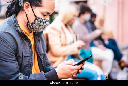 Ragazzo asiatico che utilizza smartphone coperto da maschera facciale Covid Second WAVE - nuovo concetto di stile di vita normale con le persone guardare notizie sul telefono cellulare Foto Stock