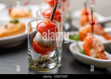 Pomodori ciliegini e crostini di mozzarella su spiedini in un bicchiere vetro con sfondo di gamberi del re in primo piano Foto Stock