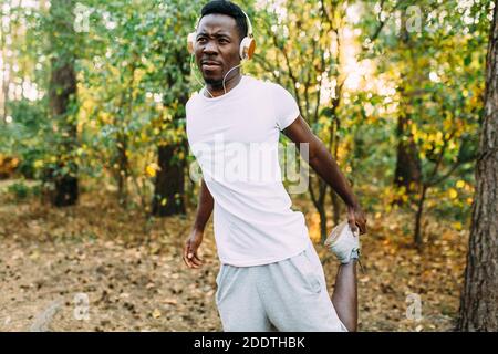 Atletico afroamericano, corridore che fa esercizi di stretching, preparandosi per l'allenamento mattutino nel Parco Foto Stock