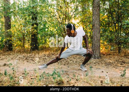 Atletico afroamericano, corridore che fa esercizi di stretching, preparandosi per l'allenamento mattutino nel Parco Foto Stock