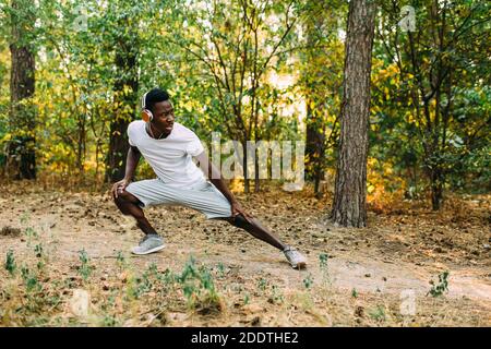 Atletico afroamericano, corridore che fa esercizi di stretching, preparandosi per l'allenamento mattutino nel Parco Foto Stock