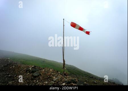 Vecchio ventoso a strisce rosso-bianco, indicatore della forza e della direzione del vento nelle montagne del Caucaso nella nebbia, cresta Aibga, escursione, trekking, Foto Stock