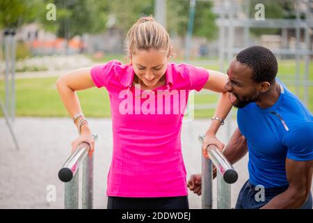 Afro american fitness istruttore istruire donna aiutare a fare push-up su Stazione a barra orizzontale a montaggio incrociato nel parco - giovane fitness trainer aiuta b Foto Stock