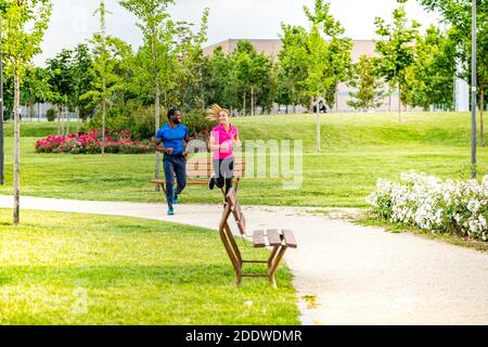 Una giovane coppia fa jogging nel parco per correre insieme. Afro americano uomo e bella ragazza bionda in abbigliamento sportivo che corre attraverso il toget del parco cittadino Foto Stock