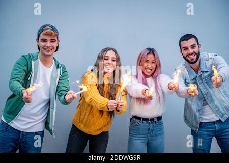 Gruppo di amici multietnici che si accalcano con sparklers - quattro teneegers festa con gli sparklers nelle loro mani Foto Stock