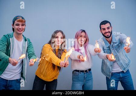 Gruppo di amici multietnici che si accalcano con sparklers - quattro teneegers festa con gli sparklers nelle loro mani Foto Stock