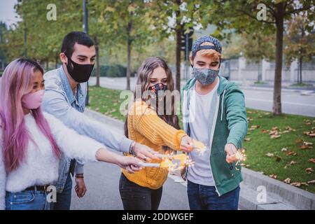 Gruppo di amici multietnici che si accecano con gli sparklers e indossano il viso maschere di sicurezza mantenendo la distanza sociale durante il tempo di coronavirus - Covid-19 spr Foto Stock