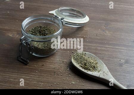 un mestolo di legno e un vaso di vetro con origano essiccato Foto Stock