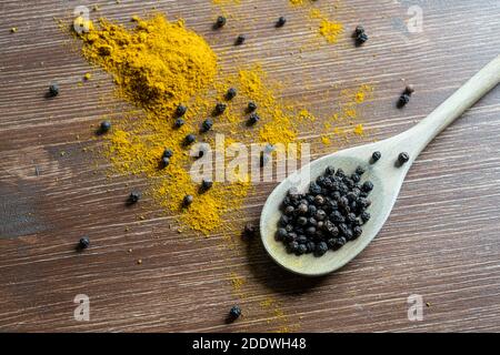 un mestolo di legno con curry in polvere e pepe in grani Foto Stock
