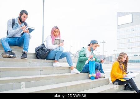 Giovani studenti universitari durante la pandemia del coronavirus. Quattro studenti universitari multi-etnici con maschere protettive all'aperto Foto Stock