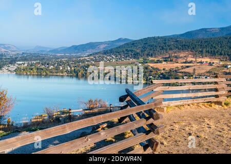 La vista da dietro una recinzione in legno del lago e le colline coperte di alberi verdi, campi, e l'erba gialla d'autunno. Le case private e blu Foto Stock