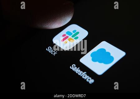 App Slack and Salesforce sullo schermo dello smartphone e una punta di un dito sopra una di esse. Concetto di fusione aziendale. Foto Stock