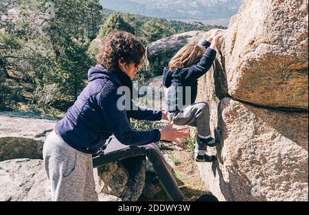 Foto d'inventario di una donna che aiuta la sua giovane figlia a salire su una roccia in montagna. Foto Stock