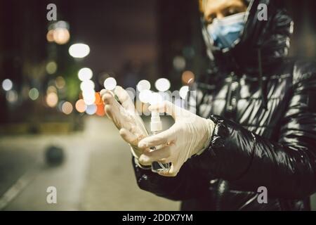 Protezione coronavirus e covid 19. Antisettico contro l'infezione in mani di donna matura su strada in città sera in inverno. Donna anziana in maschera Foto Stock