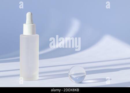 Siero anti invecchiamento con collagene e peptidi su superficie blu con ombre. Olio di acido ialuronico mockup. Luce del sole e ombra dal cosmetic del siero Foto Stock