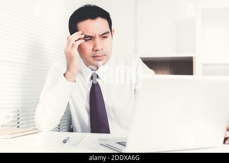 L'uomo d'affari asiatico che ottiene stressato (sconvolto) al lavoro, mettendo la sua mano sul tempiale Foto Stock