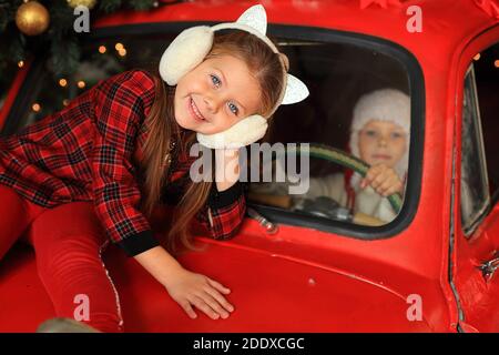 Bambini sullo sfondo di un'auto rossa con regali di Capodanno. Ragazzo e ragazza che guidano una macchina a Natale. Un sacco di regali sulla macchina di Natale Foto Stock