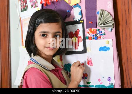 Felice sorridente indiano scuola ragazzina studente imparare disegno decorando bacheca in sala classe d'arte, bambino che indossa la scuola uniforme India. Istruzione Foto Stock