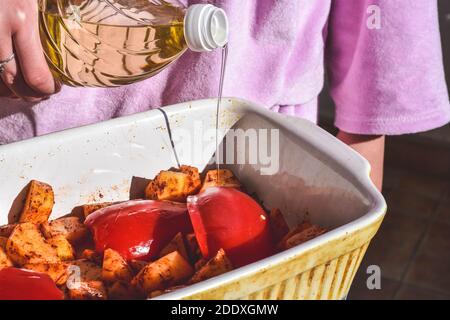 Lo chef versa l'olio da cucina dalla bottiglia su patate grezze/cibo preparazione/ Foto Stock