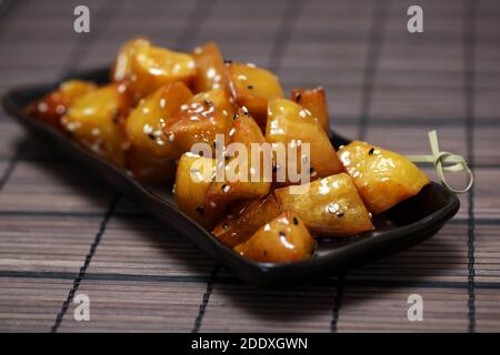 Patate dolci candite, Daigaku IMO, cibo tradizionale giapponese patate dolci fritte e ricoperte di sciroppo dolce sul piatto nero. Patate dolci fritte Foto Stock