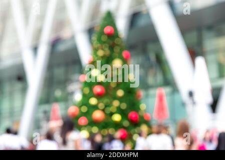 Immagine offuscata dell'albero di Natale decorato colorato all'aperto con la gente di fronte al centro commerciale durante le feste Foto Stock