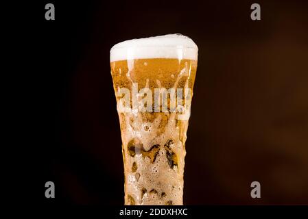 Bicchiere di bevanda alcolica di birra fredda dorata con schiuma traboccante bolle nella barra Foto Stock