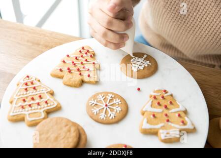 Giovane donna che decora biscotti natalizi fatti in casa con pan di zenzero e glassa reale zucchero su piatto bianco Foto Stock