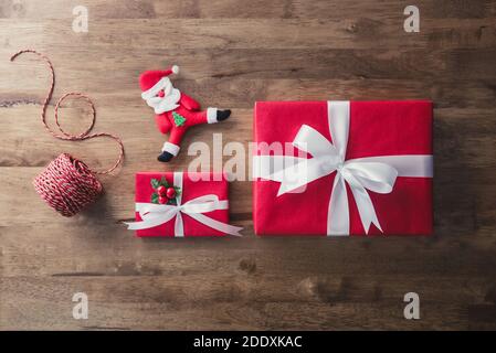 Vista dall'alto delle colorate scatole regalo natalizie rosse con bambola Babbo Natale e spago decorativo sullo sfondo del tavolo in legno, vista dall'alto Foto Stock