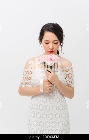 Profilo ritratto di una bella giovane donna che odora rosa e guarda verso il basso, isolata su sfondo bianco. Foto Stock