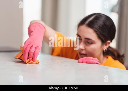 Ritratto offuscato di una giovane donna in guanti di gomma sta strofinando il tavolo con uno straccio. Primo piano. Pulizia della casa. Foto Stock