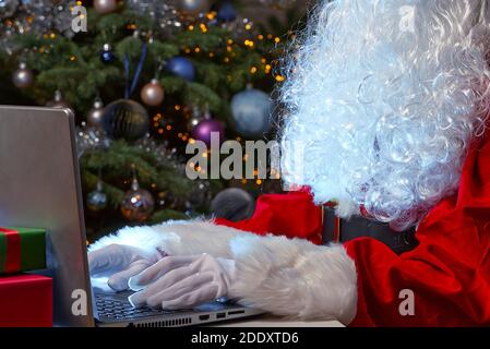santa seduta dietro il computer portatile. Babbo Natale in un blocco seduto dietro un computer portatile conduce la comunicazione online. Foto Stock
