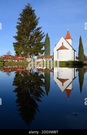 Saalau, Germania. 24 Nov 2020. La cappella sulla piazza del villaggio di Saalau, alberi e case si riflettono in uno stagno. Il villaggio nel nord del distretto di Bautzen nella Sassonia orientale appartiene alla città di Wittichenau dal 1994. Si trova nel paesaggio delle brughiera e degli stagni dell'alta Lusazia e fa parte dell'area degli insediamenti sorbiani. Credit: Robert Michael/dpa-Zentralbild/ZB/dpa/Alamy Live News Foto Stock