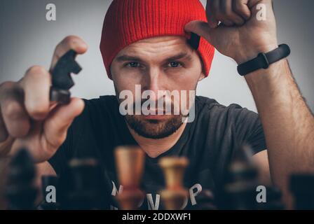un giocatore di scacchi in un cappello rosso muove un nero cavaliere che guida il re bianco in un angolo Foto Stock