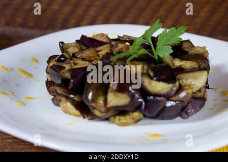 Piatto di melanzane a dadini su una crema di pomodori ciliegini gialli in un piatto bianco. Legno di fondo. Messa a fuoco selettiva. Foto Stock