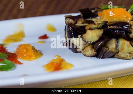 Piatto di melanzane a dadini su una crema di pomodori ciliegini gialli e rossi in un piatto bianco. Legno di fondo. Messa a fuoco selettiva. Foto Stock
