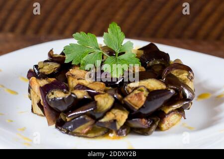 Piatto di melanzane a dadini su una crema di pomodori ciliegini gialli in un piatto bianco. Legno di fondo. Messa a fuoco selettiva. Foto Stock