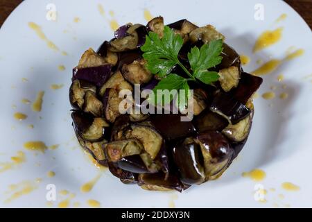 Piatto di melanzane a dadini su una crema di pomodori ciliegini gialli in un piatto bianco. Legno di fondo. Messa a fuoco selettiva. Foto Stock