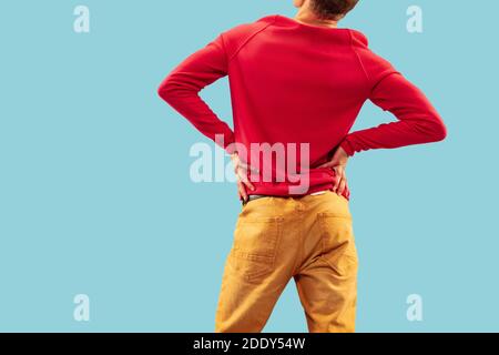 Giovane uomo in abiti colorati alla moda che si posano su sfondo blu studio. Vista posteriore Foto Stock