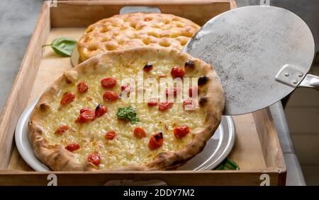 Pizza italiana con pomodori ciliegini e mozzarella, particolare della pala da forno che scarica la pizza appena sfornata su vassoio di legno Foto Stock