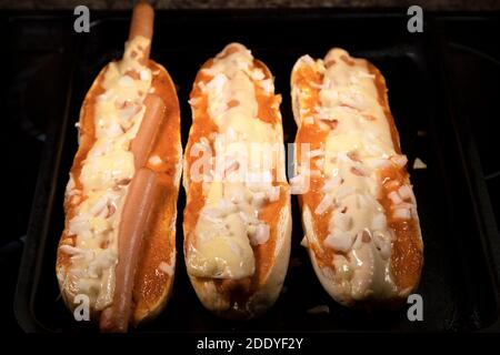 Hot dog spagnoli freschi dal forno. I hot dog sono stati messi in baguette e cotti con formaggio e cipolle tritate. Foto Stock