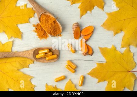 Fondo piatto con curcuma in diverse forme pillole e polvere In un cucchiaio di legno e radice tagliata in pezzi impilati immagine Foto Stock