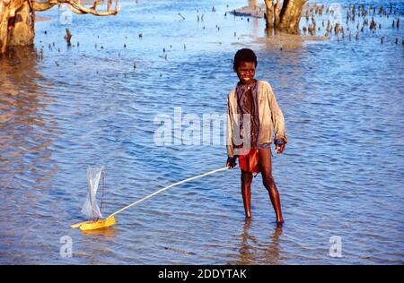 Sorridente malgascio o Madagacan Vezo Boy giocando con una casa Modello Pirogue o Outrigger Canoe nelle Arche di A. Foresta di mangrovie sulla costa a nord di Tulear o Toliara Madagascar Africa Foto Stock
