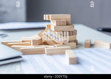 Vista ravvicinata di blocchi di legno gioco costrizione collassare con scritta sul copyright con luogo di lavoro sfocato sullo sfondo Foto Stock