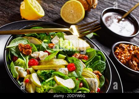 insalata di pere con cubetti di formaggio blu, broccoli, foglie di spinaci, noci caramellate e semi di melograno su un piatto nero su un tavolo di legno, thanksgivi Foto Stock