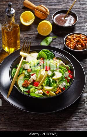 insalata di pere con cubetti di formaggio blu, broccoli, foglie di spinaci, noci caramellate e semi di melograno su un piatto nero su tavola di legno, ringraziamento Foto Stock