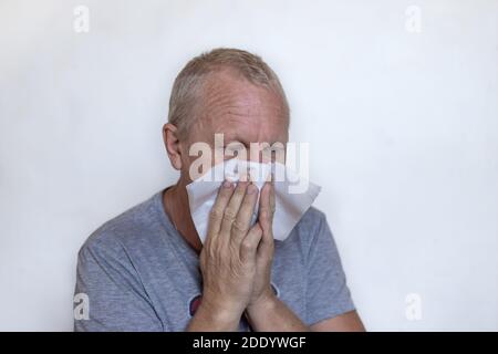 Un uomo europeo anziano gli soffia il naso, gli starnuti e le tosse in un tovagliolo. Infezione da coronavirus. Foto Stock