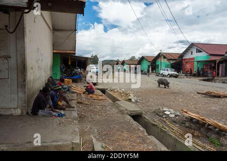 Mercato di un grande mercato alla periferia di Wamena, Papua occidentale, Indonesia. Uomini seduti contro il muro in attesa di un lavoro. Foto Stock